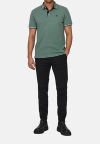 Groene polo shirt met een zwarte kraag, witte accenten, slim fit, gecombineerd met zwarte broek en zwarte schoenen. Heeft een logo op de borst.