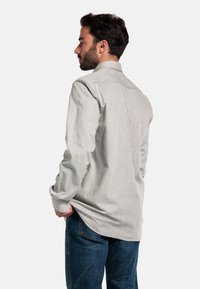 Lichtgrijs overhemd met lange mouwen en een kraag, gedragen ongebd, met een gestructureerde stof en knoopmanchetten, gecombineerd met donkerblauwe jeans.