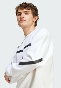 Biely sveter s čiernymi horizontálnymi prúžkami, okrúhlym výstrihom a rebrovanými manžetami. Materiál má textúrovaný povrch a voľný strih.