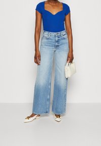 Royal blue ribbed bodysuit with a square neckline, paired with light blue wide-leg jeans. White pointed toe shoes and a small white handbag.