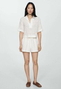 Witte cropped shirt met een kraag en korte mouwen, gecombineerd met bijpassende shorts met trekkoord. Beide hebben een ruitpatroon en een gestructureerde stof.