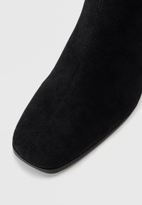 Svart mockaskinnsankleboot med fyrkantig tå och synlig söm som löper längs mitt fram.