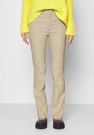Personne portant un pantalon beige droit, un pull en tricot jaune et des chaussures à plateforme marron avec des semelles noires.
