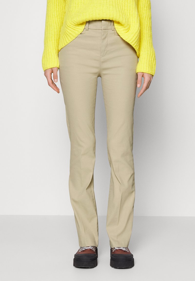 Personne portant un pantalon beige droit, un pull en tricot jaune et des chaussures à plateforme marron avec des semelles noires.
