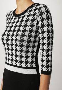 Robe en tricot noir et blanc avec motif pied-de-poule, encolure ronde, manches trois-quarts et ceinture noire unie.