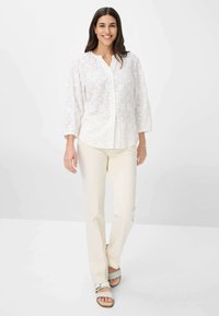 Weißes Hemd mit Blumenstickerei, kombiniert mit kremfarbenen Hosen und hellen Sandalen, mit einem lockeren Schnitt und Dreiviertelärmeln.