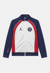 Chaqueta con cremallera que presenta un cuerpo principal blanco, mangas azul marino y acentos rojos. Incluye un logo de Jordan y un emblema del club de París. Textura suave.