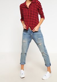 Röd och svart rutigt skjorta med knappar, kombinerad med ljusblå slitna jeans och vita sneakers; avslappnad passform och uppvikt byxben.