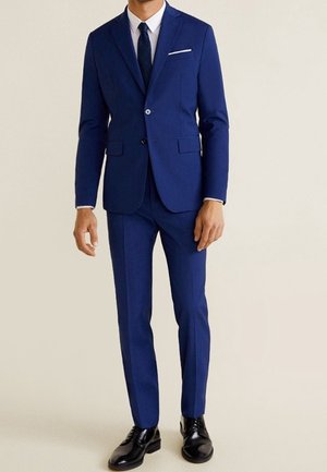 Completo blu navy realizzato in un tessuto liscio, caratterizzato da un taglio slim fit, giacca monopetto, revers a nozze e pantaloni coordinati. Scarpe nere completano il look.