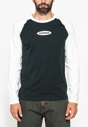 Uomo con maglia a maniche lunghe bianca e nera con logo "CARRERA" sul petto, abbinata a jeans grigio scuro.