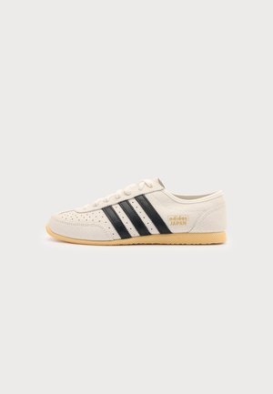 Sneaker bianca Adidas Japan con strisce nere e suola in gomma mostrata di profilo su uno sfondo chiaro e uniforme.