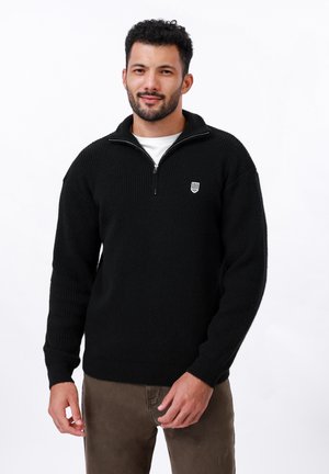 Schwarzer, gerippter Strickpullover mit einem Halbreißverschluss-Kragen und einem kleinen weißen Logo auf der Brust. Hat lange Ärmel und eine lockere Passform.