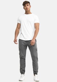 Wit katoenen T-shirt gecombineerd met grijze cargobroek met elastische manchetten, zijzakken en een taille met koord. Draagt witte sneakers.