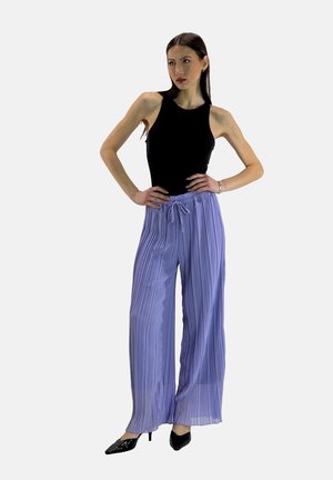 Zwarte mouwloze top gecombineerd met lichtpaarse geplooide wijde broek met een trekkoord in de taille. Model draagt zwarte puntige hakken.