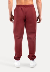 Bordové tepláky s elastickým pasem a manžetami. Vyrobené z hladké látky. Mají boční kapsy a volnější střih.