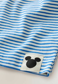 Bavlnená látka s striedavými modrými a bielymi horizontálnymi pruhmi. V rohu sa nachádza čierny logo Mickey Mouse na bielej nálepke.