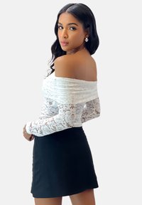 Top blanco de encaje sin hombros con un patrón texturizado, combinado con una minifalda negra ajustada. Diseño simple y moderno con mangas largas.