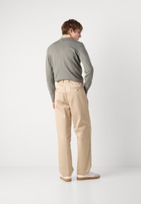 Beige, högmidjade byxor med rak passform, med bakfickor och en knappdetalj, i kombination med en ljusgrå stickad tröja.