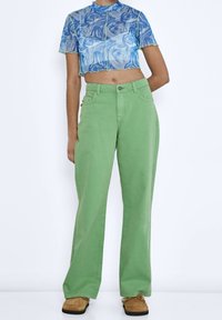 Pantaloni a gamba larga verdi realizzati in cotone, con vita alta, tasche laterali e una semplice chiusura a bottone. Abbinati a un top corto blu marmorizzato.