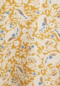 Kangas med en senapsgul bakgrund med vita paisleymönster, blå blommor och gyllene accenter. Designen har en texturerad yta.