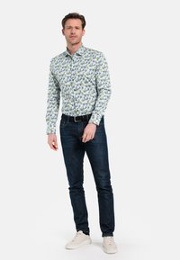 Bloemige button-up shirt in lichte kleuren met groene en blauwe patronen. Gecombineerd met donkere jeans en witte sneakers.