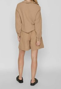 Hnědý texturovaný dlouhý rukáv s límcem, doplněný o odpovídající šortky a černé nazouvací boty. Jednoduchý design, uvolněný střih.