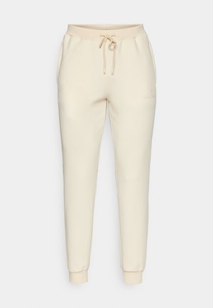 Beżowe spodnie dresowe z ściągaczem w talii, zwężającymi się nogawkami i prążkowanymi mankietami. Posiada subtelny detal z logo na przedniej lewej udzie.