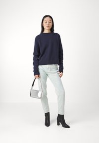 Marineblå strikkegenser, lyseblå jeans og svarte hælboots. Sølvveske med svart stropp, slank design og glansfull tekstur.