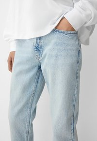 Jeans din denim albastru deschis cu o croială lejeră, având un design tipic cu cinci buzunare și o ușoară decolorare. Asortate cu un top alb cu mânecă lungă.