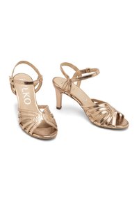 Sandales à talons hauts dorées métalliques avec un bout ouvert, arborant des accents horizontaux ondulés et un talon aiguille fin.