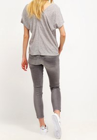 Top gris de manga corta con espalda en V, combinado con jeans gris ajustados y zapatillas blancas con detalles metálicos en el talón.