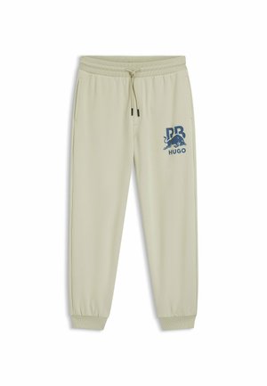 Helle beigefarbene Sweatpants mit elastischem Bund und Bündchen, versehen mit einem blauen Grafiklogo auf dem linken Oberschenkel. Glatte Stoffstruktur.