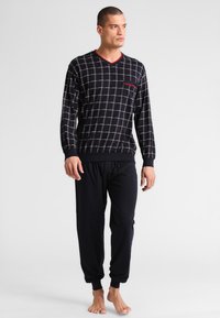 Heren lounge set met een marineblauwe lange mouw top met een ruitpatroon en rode accenten, gecombineerd met effen zwarte elastische broek met tailleband.