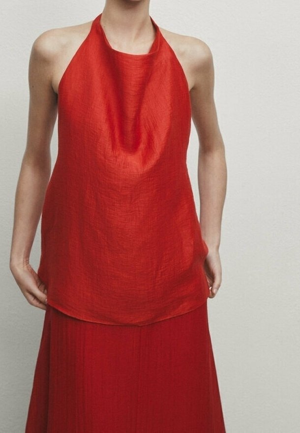 Personne portant un haut rouge sans manches à col halter et une jupe rouge assortie sur un fond clair uni.