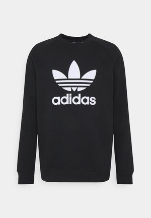 Sudadera negra de manga larga con cuello redondo y un gran logo blanco de trébol de Adidas junto con texto centrado en el frente.