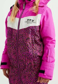 Ljusrosa och vit snöjacka med leopardmönstrad nedre del, dragkedja framtill, svart logga "Destination Snow" och justerbara handledsremmar.