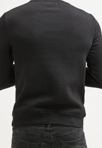 Czarna bluza z okrągłym dekoltem, długimi rękawami i ściągaczami przy mankietach. Miękka tkanina; minimalistyczny design, bez widocznych logotypów czy wzorów.