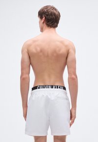 Λευκά μαγιό σορτς με μαύρη ζώνη μέσης Calvin Klein, με ομαλή υφή και μια  μικρή πίσω τσέπη με φερμουάρ.