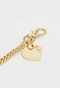 Portachiavi in oro con un gancio e un tag a forma di cuore con un design a spirale, texture liscia e finitura lucida.