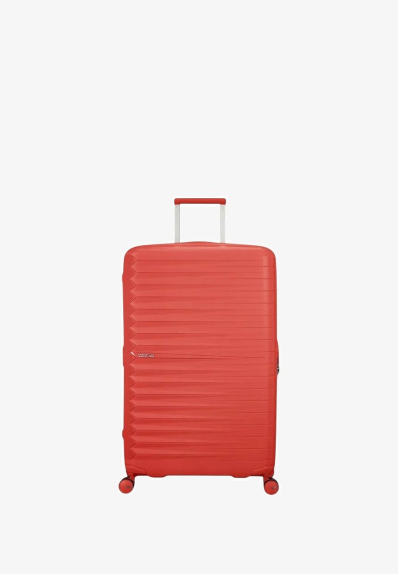 Valigia rigida rossa con un design testurizzato, caratterizzata da scanalature verticali e manico retrattile. Si muove su quattro ruote per una maggiore mobilità.