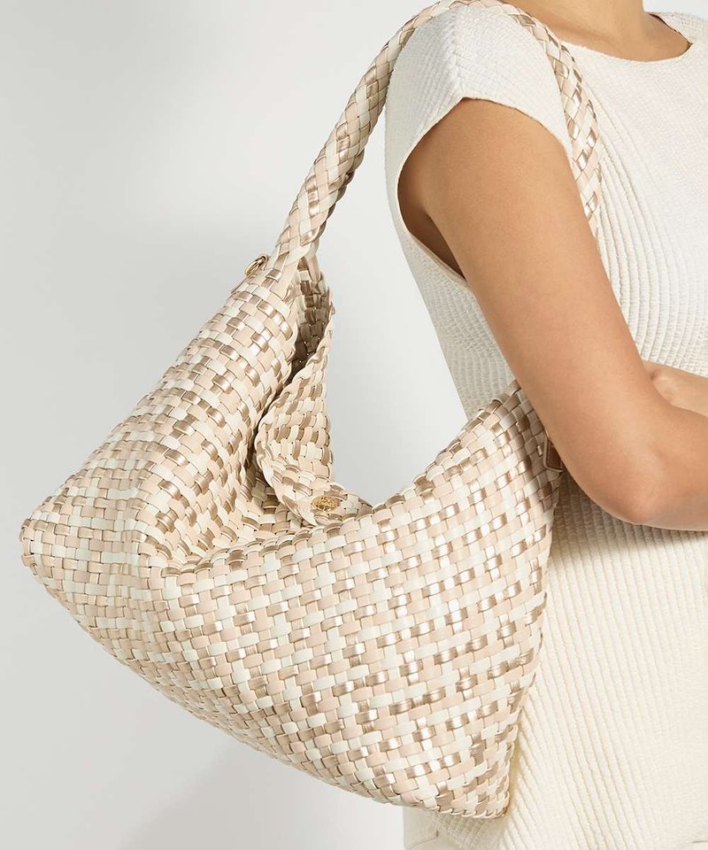 Femme portant une robe blanche et portant un grand sac à bandoulière tissé beige et crème avec une bandoulière tressée.