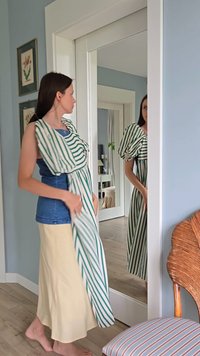 Gestreepte groene en witte jurk met pofmouwen, gelaagd over een blauwe top. De rok is eenvoudig beige en heeft een vloeiende stof met een zachte textuur.
