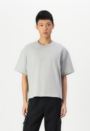 T-shirt en coton gris avec une coupe décontractée, des manches courtes et un col rond. Texture lisse, design uni, sans motifs ni accents visibles.