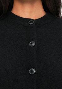Cardigan nero a maglia con scollo rotondo, caratterizzato da quattro bottoni neri e una texture morbida, che mette in risalto un design minimalista.
