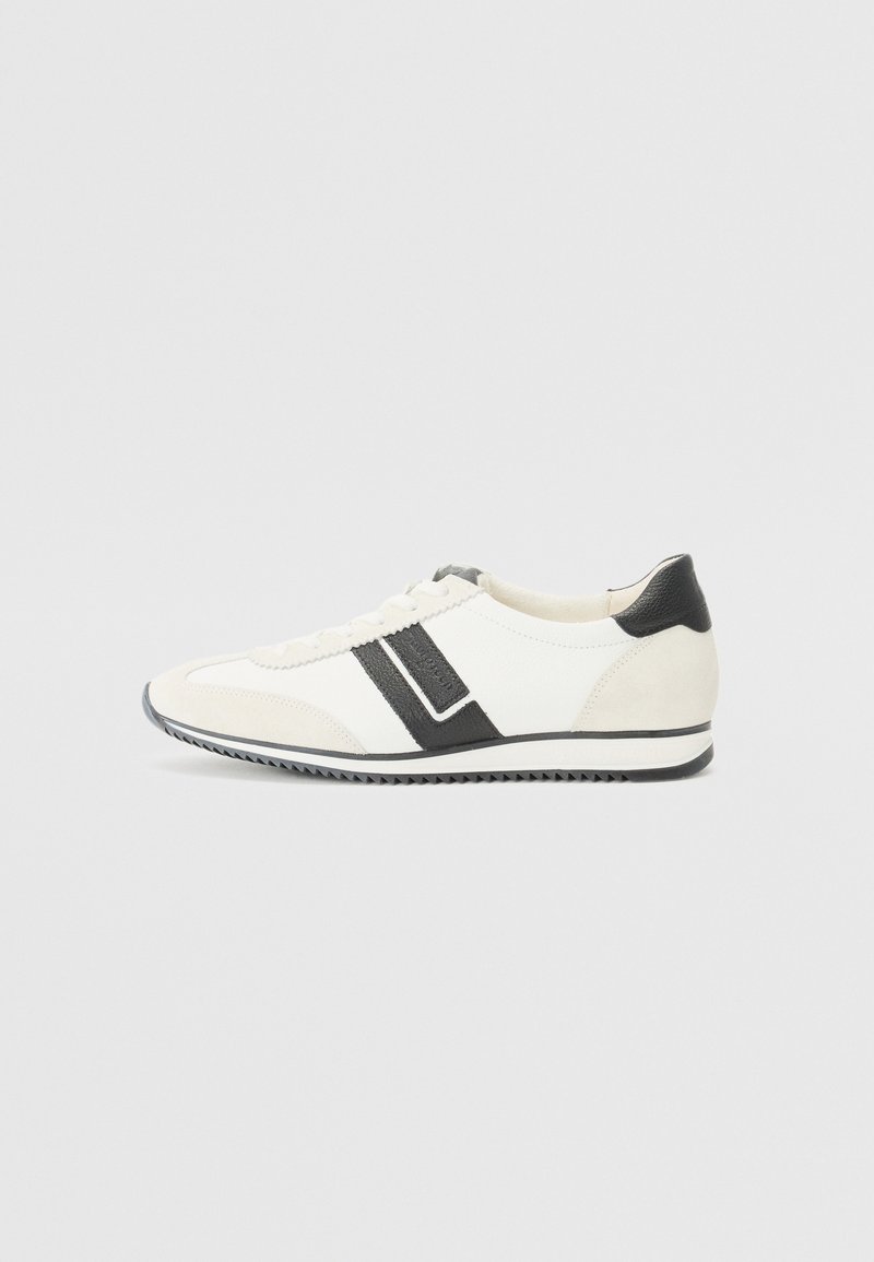 Valged ja mustad spordijalatsid, mis on valmistatud suede'ist ja nahast, omavad ümmargust ninaosa, vastandlikke jooni ja tekstureeritud kummist tallat.