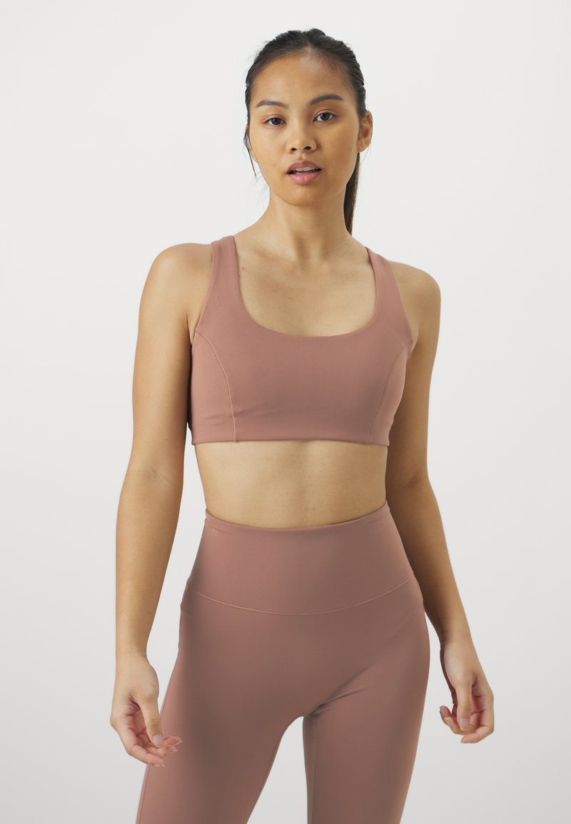 Sujetador deportivo color malva con escote cuadrado y tirantes anchos, combinado con leggings de cintura alta a juego. Tejido liso y elástico.