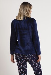 Chaqueta de forro polar azul marino con una textura suave, que presenta mangas largas y un ajuste relajado, combinada con pantalones de pijama estampados que muestran caras juguetonas.