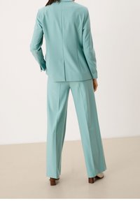 Un costume sur mesure bleu sarcelle comprenant un blazer ajusté et un pantalon à jambes larges. Tissu lisse avec légère brillance, couleur unie, et détails de boutons sur le blazer.