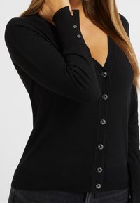 Black cardigan made of soft knit fabric, featuring a V-neck, long sleeves, and five glossy buttons down the front. Ribbed cuffs and hem.