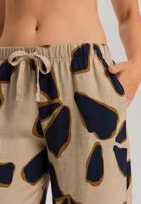 Lässige beige Hose mit auffälligen navyblauen und braunen abstrakten Mustern. Sie hat einen elastischen Bund mit Kordelzug und Seitentaschen.